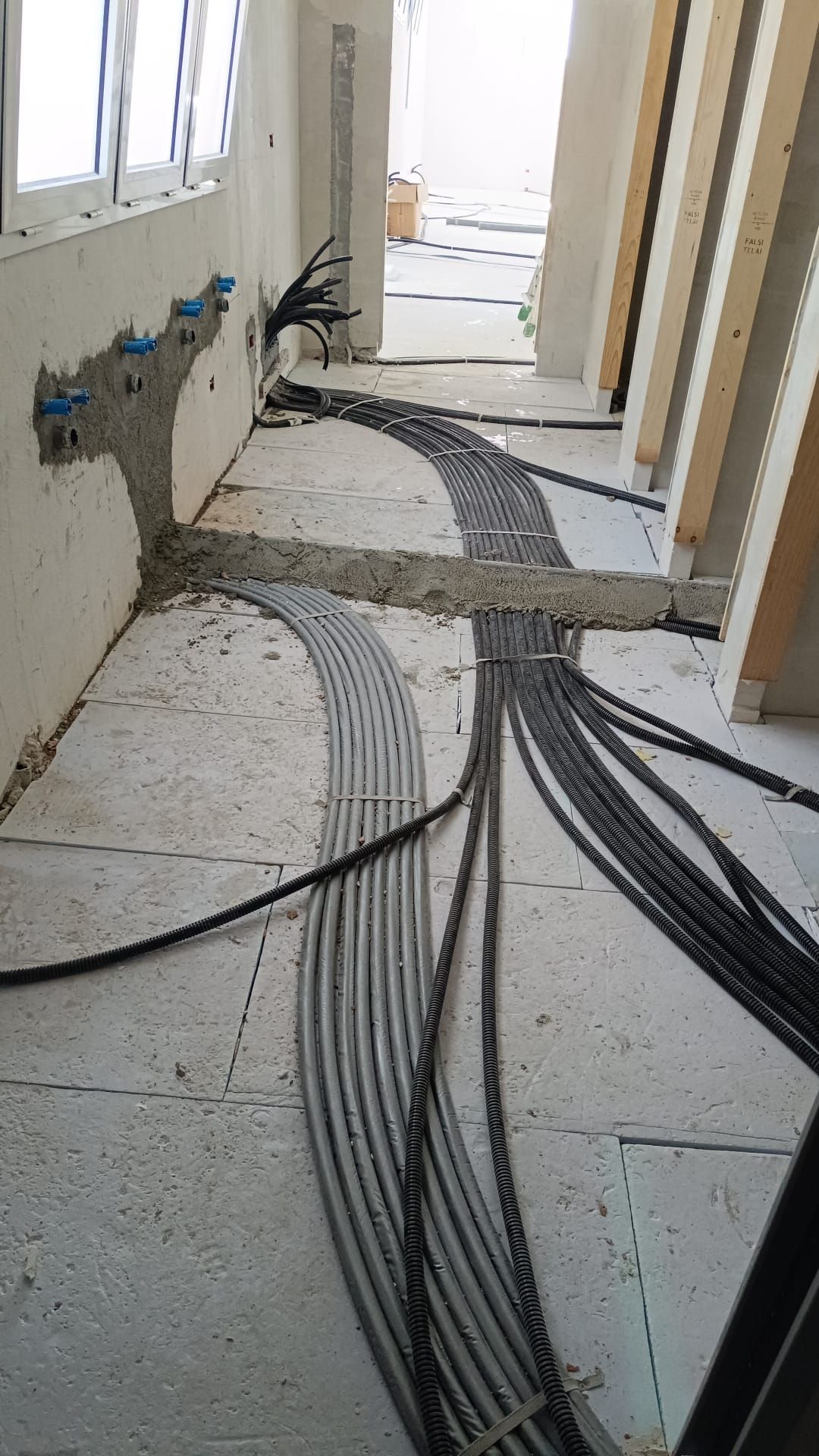 Corridoio non finito con cavi elettrici a vista che corrono lungo il pavimento e scatole di derivazione fissate alla parete.