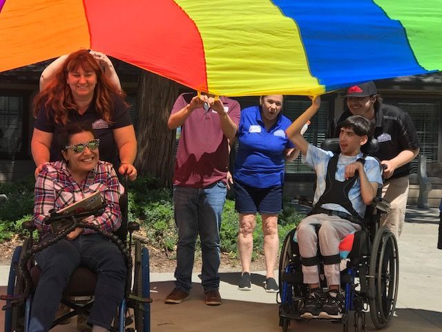 A group of people in wheelchairs holding a rainbow parachute