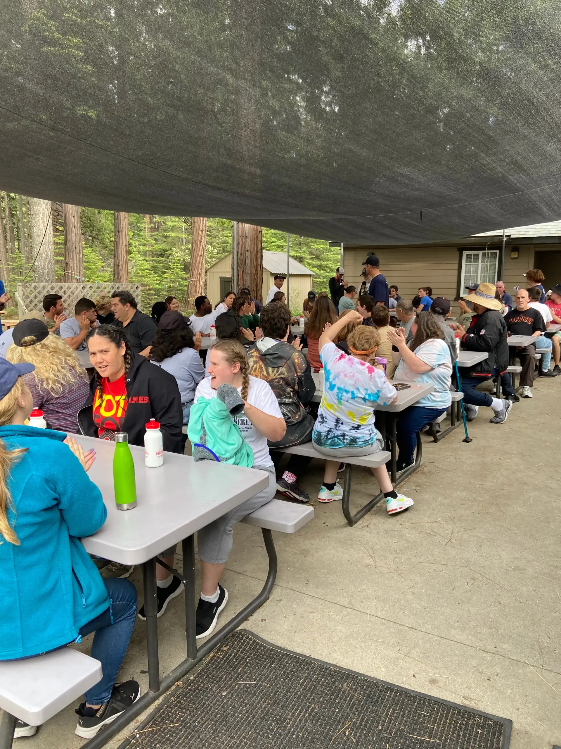 A group of people are sitting at picnic tables under a canopy.
