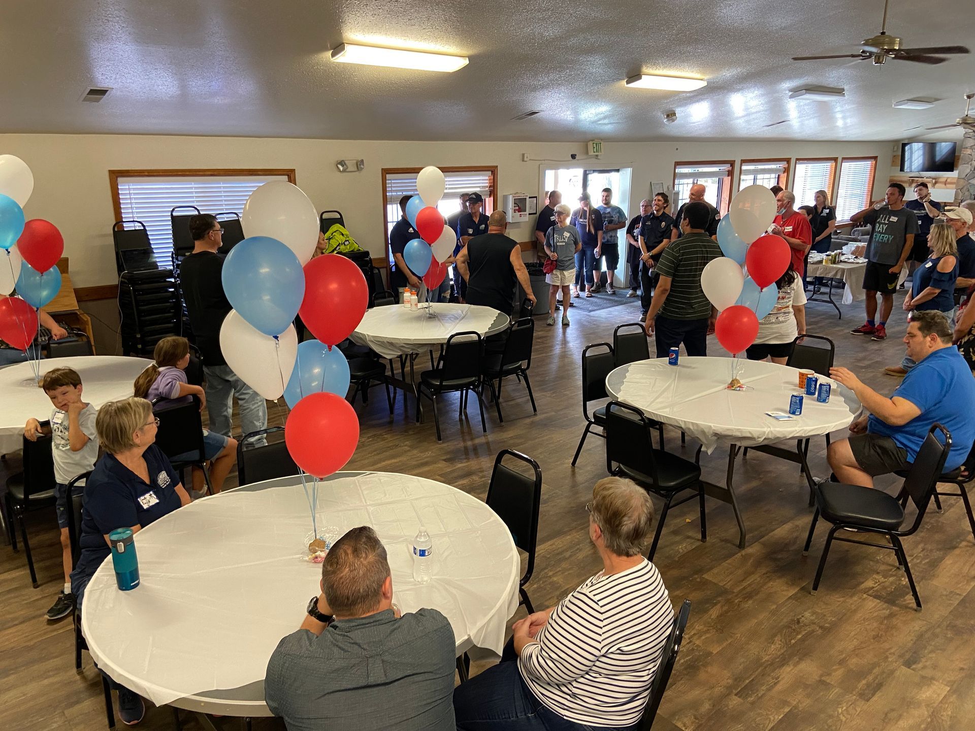 A group of people are sitting at tables in a room with balloons on them.