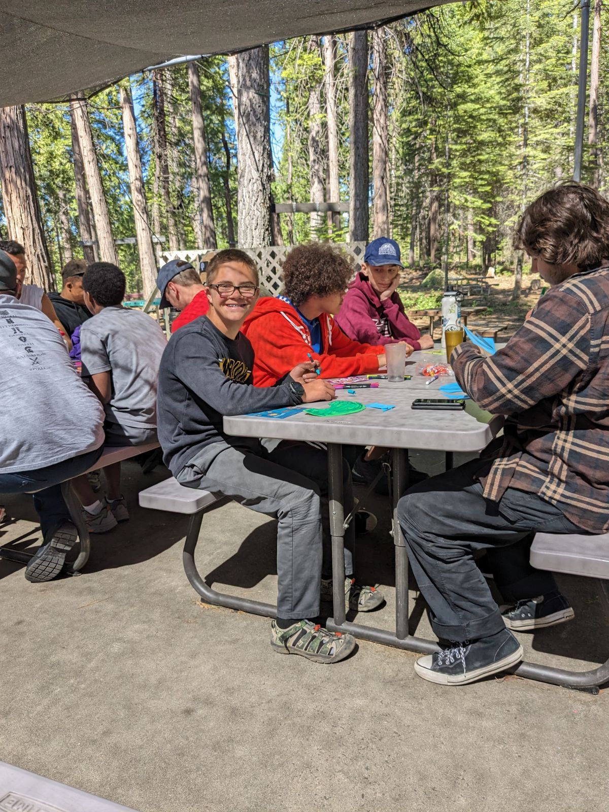 A group of people are sitting at a picnic table in the woods.