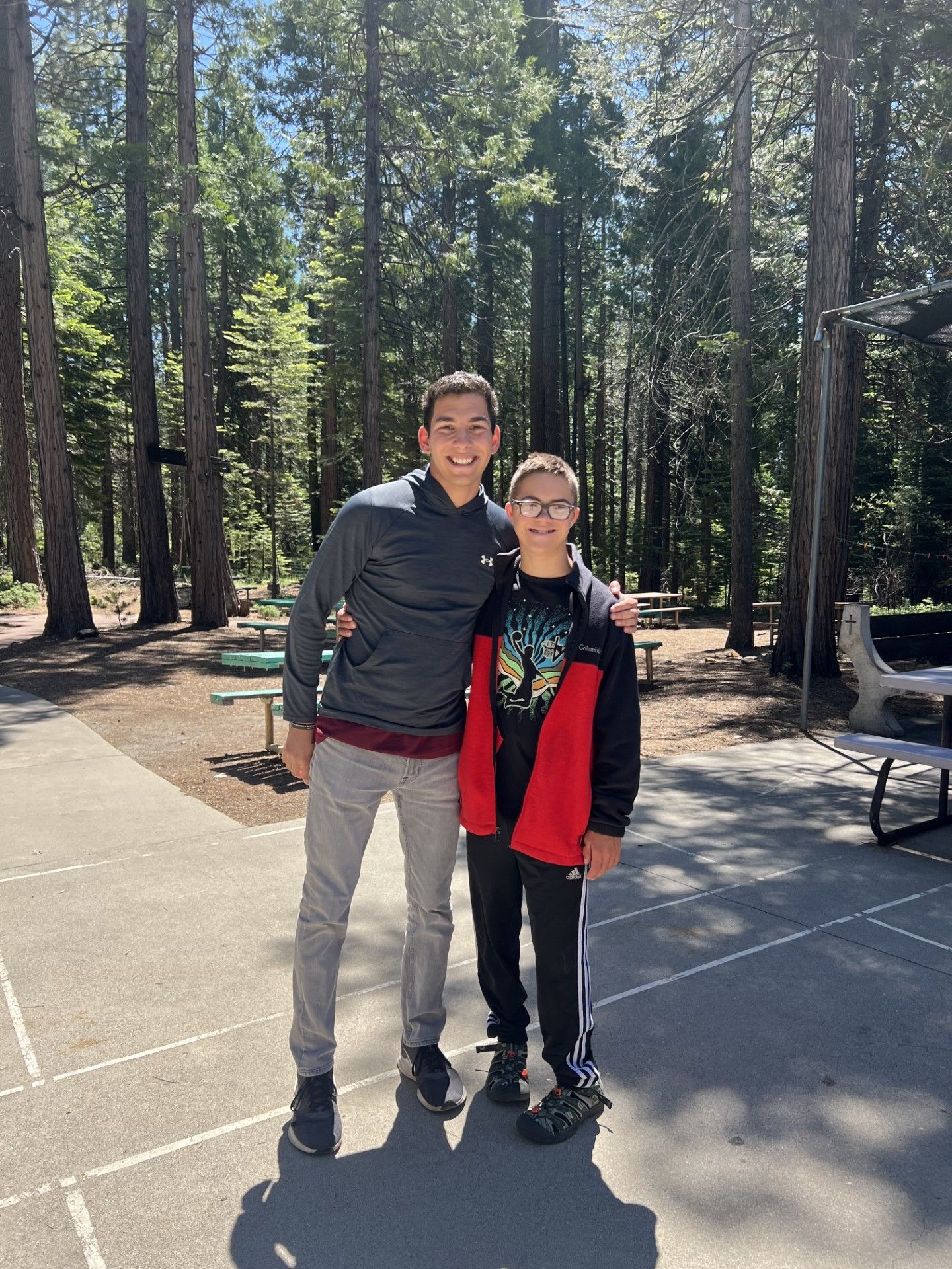 Two young men are standing next to each other in a park.
