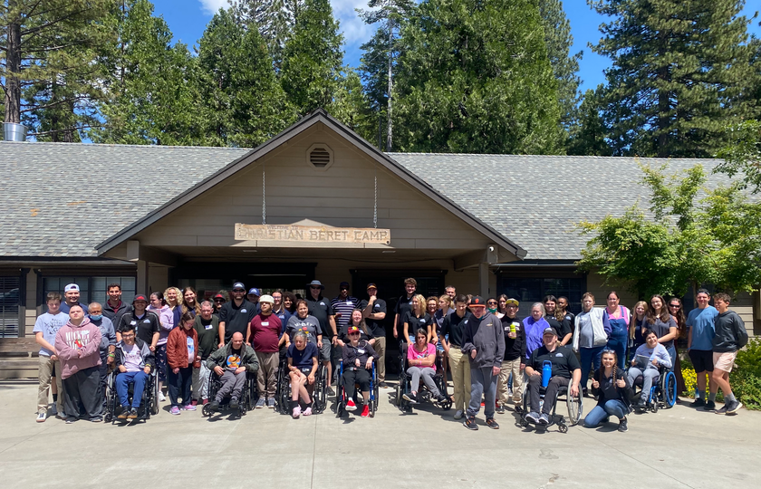 A large group of people in wheelchairs are posing for a picture in front of a building.