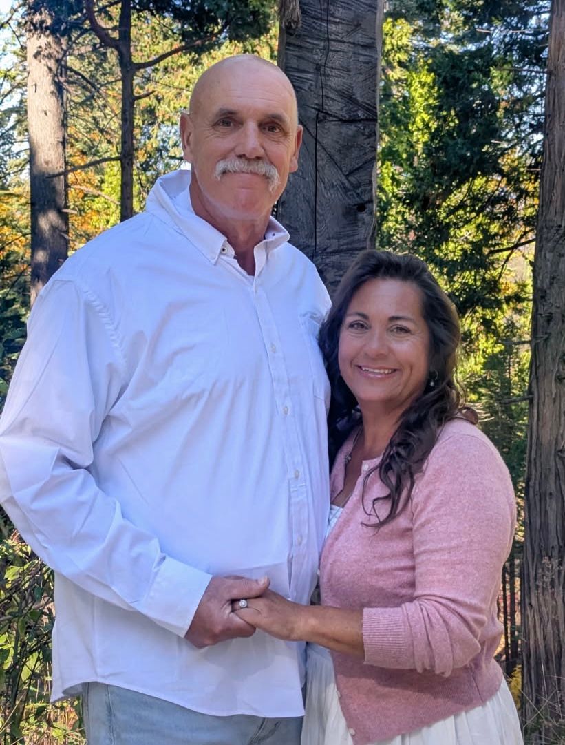 A man , woman and baby are posing for a picture in the woods.