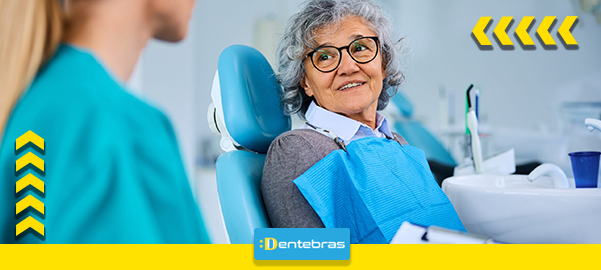 Dentista com luvas azuis examina um paciente sorridente sentado na cadeira do dentista, com setas amarelas destacando as áreas.