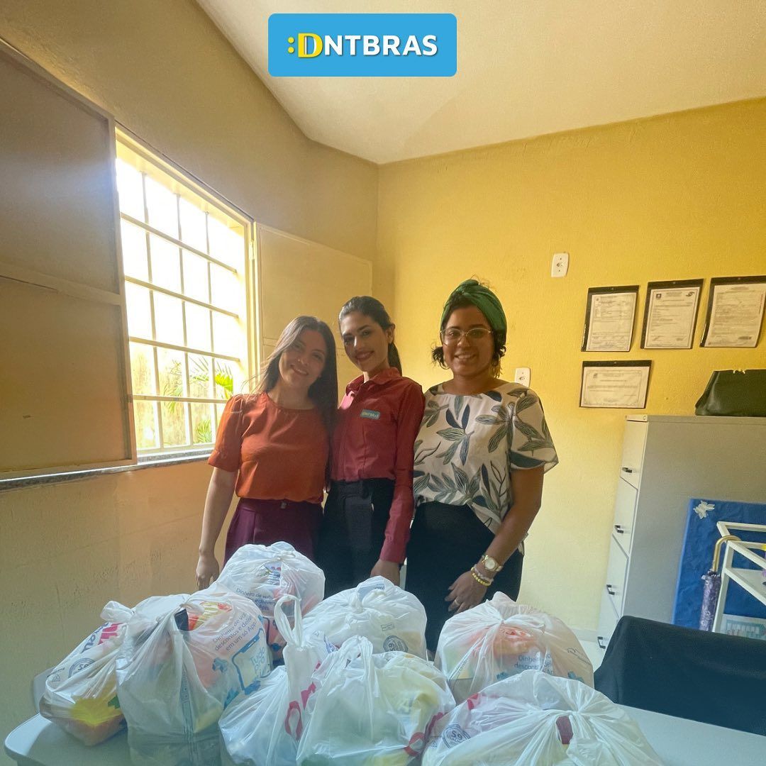 Três pessoas estão atrás de sacolas de suprimentos em uma sala iluminada com paredes amarelas e uma janela.