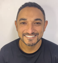 Pessoa sorridente vestindo camisa preta contra um fundo claro liso.