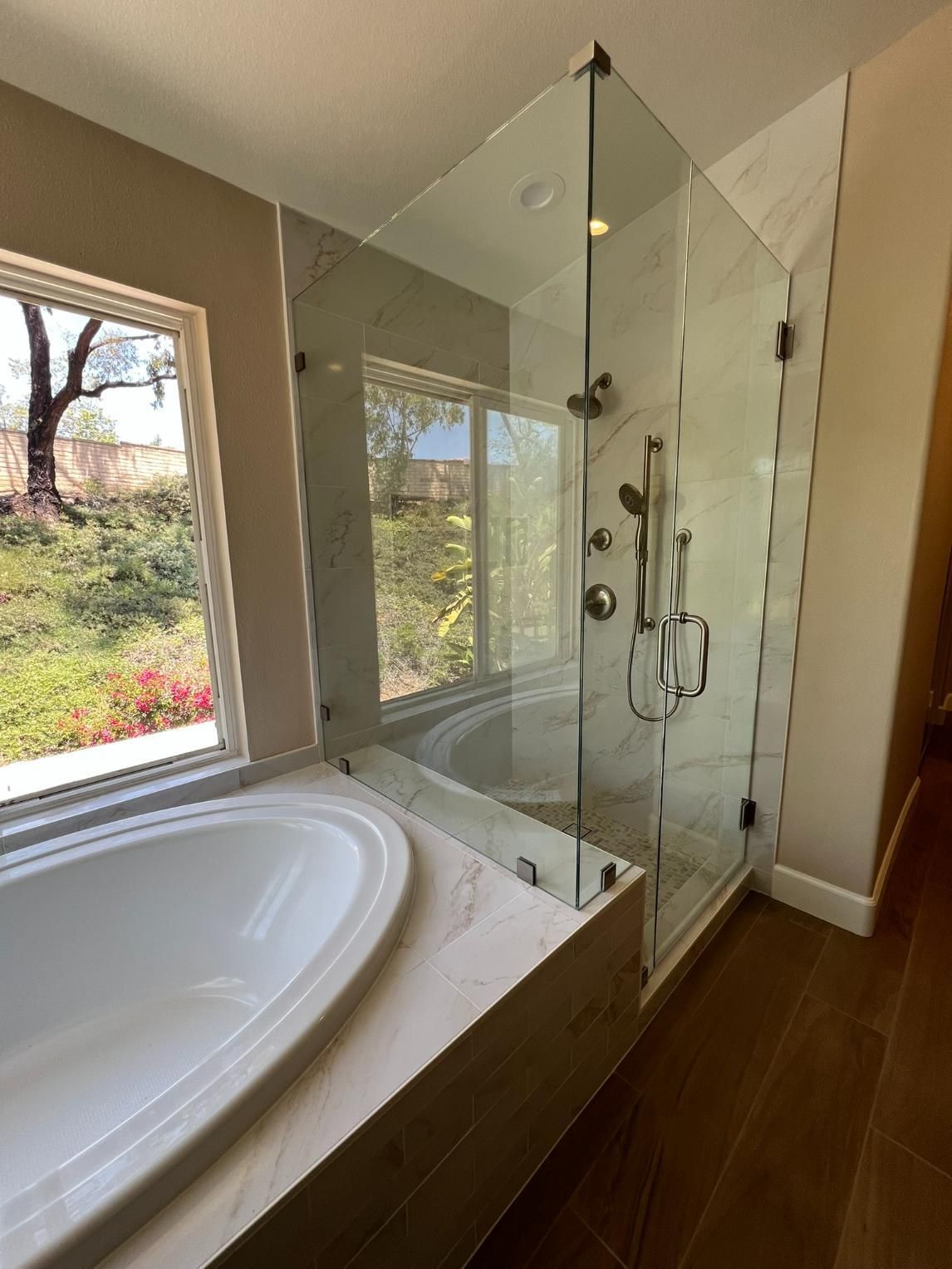 Modern bathroom with freestanding tub, glass shower, and wood floor beside a window with garden view