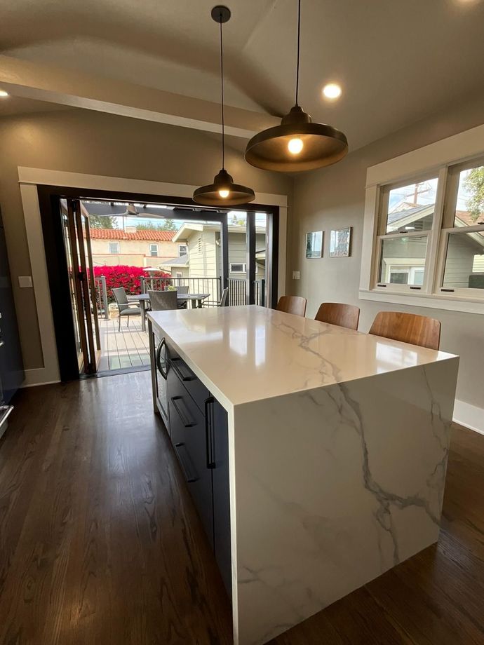 Modern kitchen with a white marble island, pendant lights, and open doors to a balcony