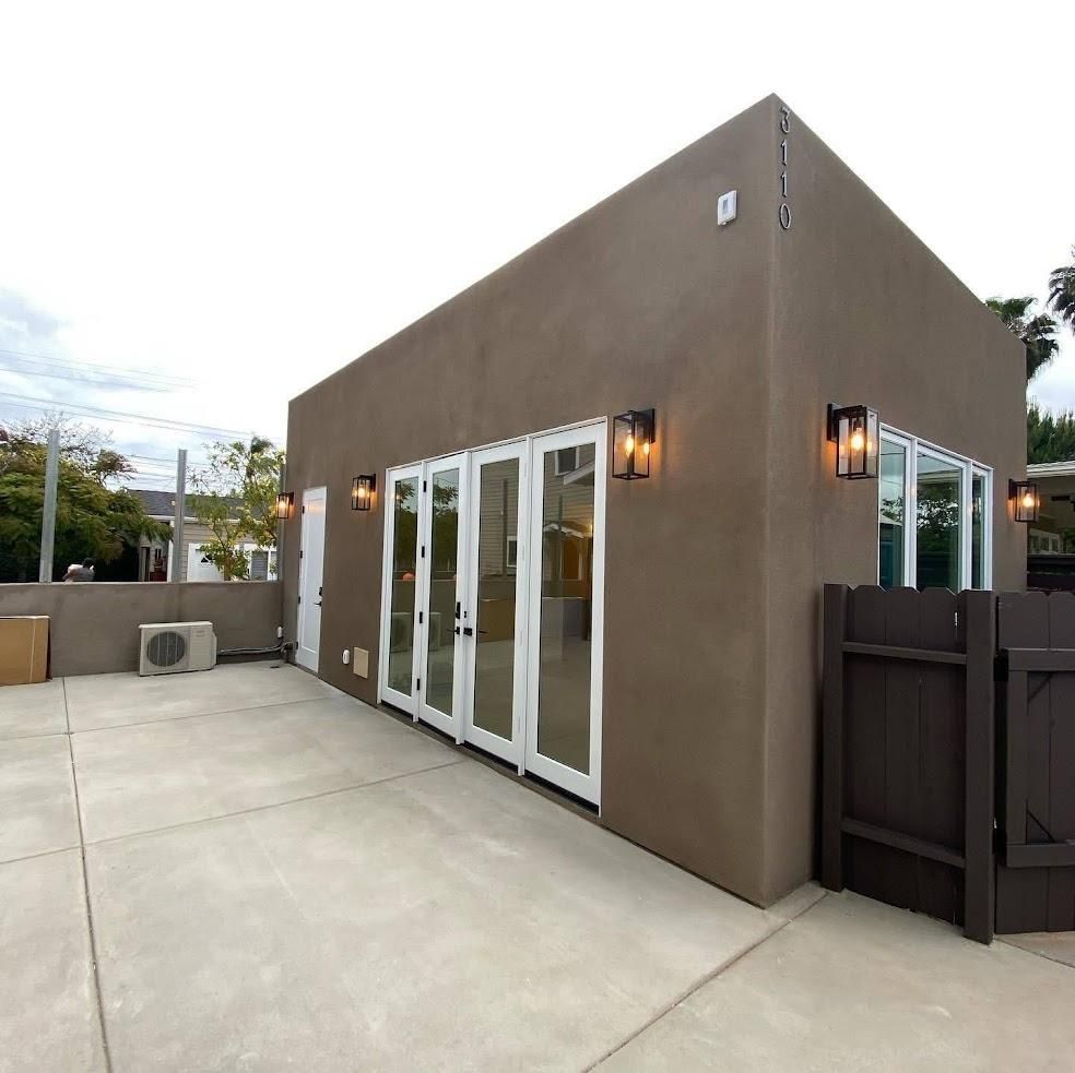 Modern tan stucco patio with white glass doors, wall sconces, and a concrete courtyard at dusk