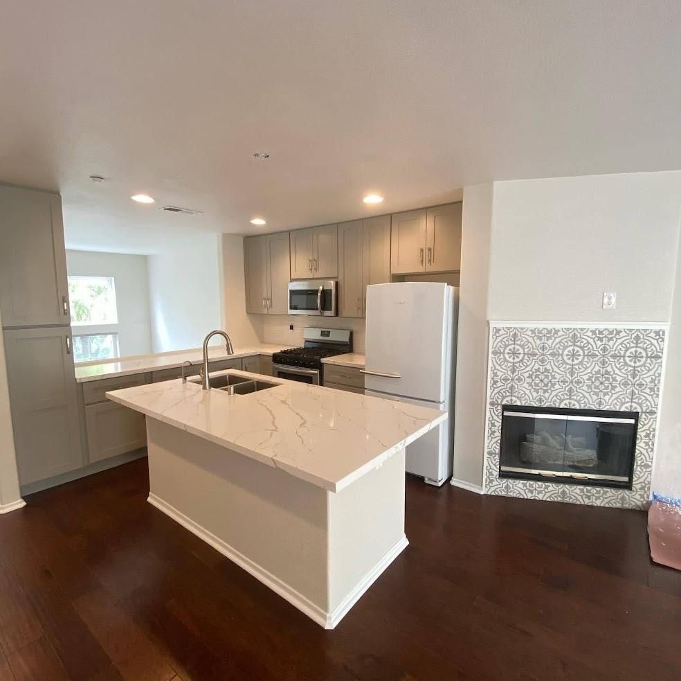 Bright modern kitchen with white island, stainless appliances, dark wood floors, and tiled fireplace wall