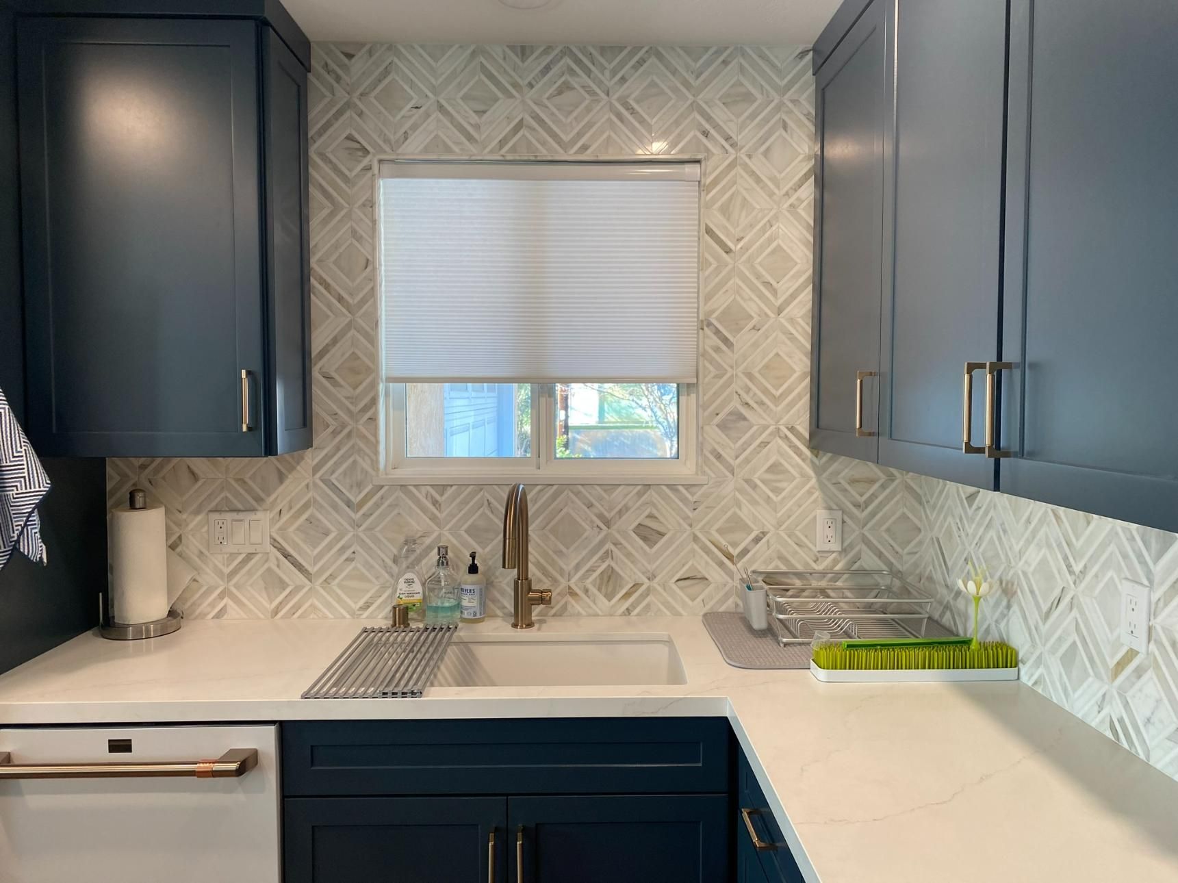 Modern kitchen with navy cabinets, white countertops, patterned backsplash, and a window over the sink