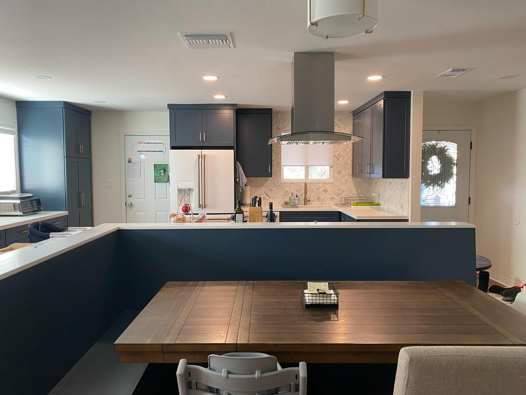 Modern kitchen with navy island, wood dining table, white cabinets, and stainless range hood