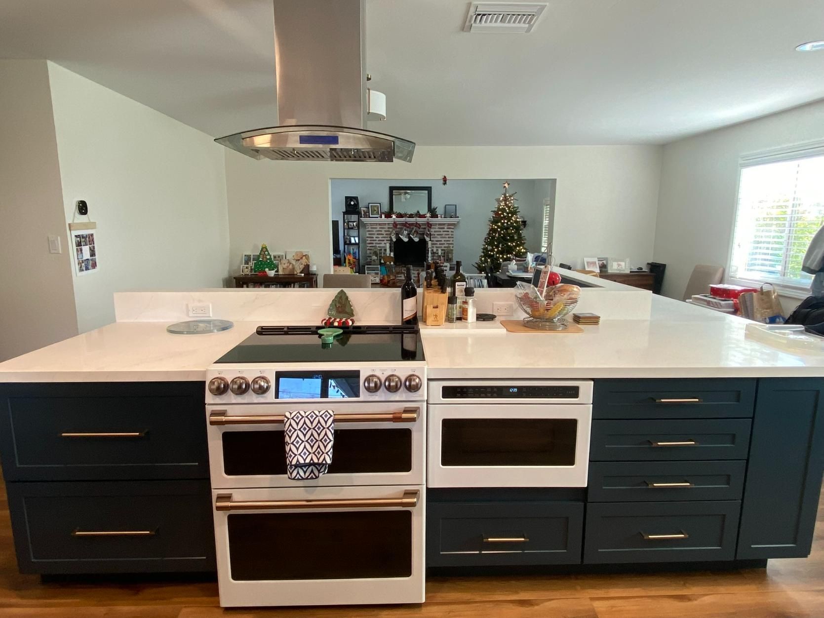 Modern kitchen with dark cabinets, white island, stainless range hood, and holiday decor in the background