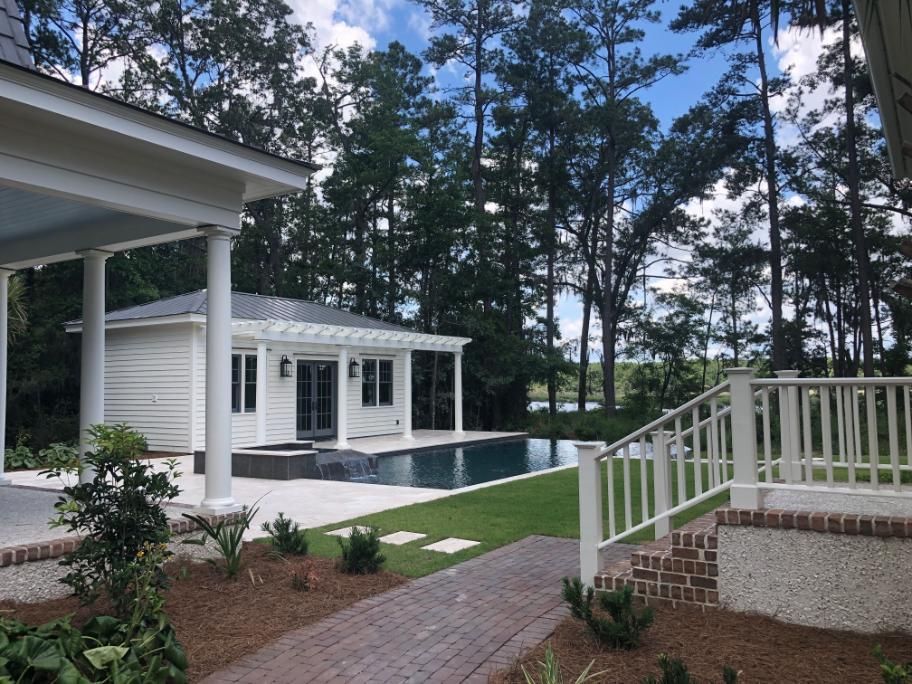Backyard patio with white pool house, swimming pool, brick walkway, and screened porch under tall trees