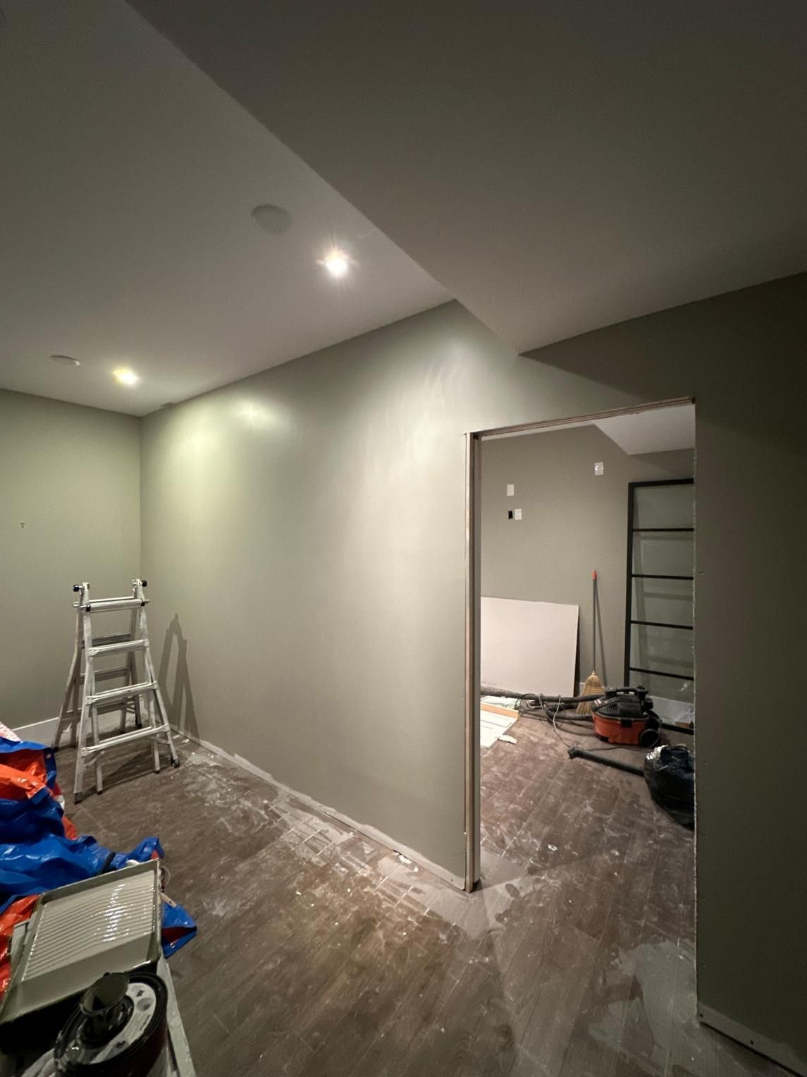 Renovated room with gray walls, recessed lights, ladder, and construction tools on a dusty floor.