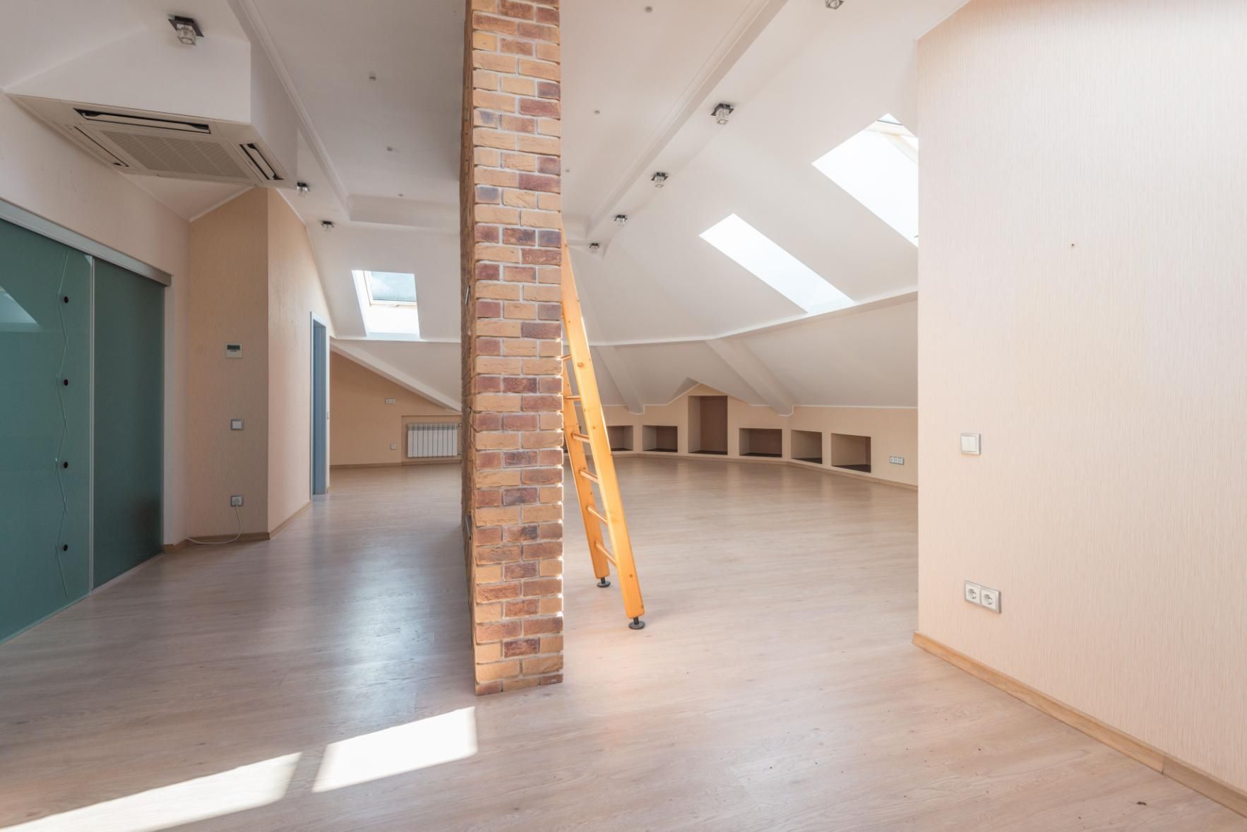 Empty loft interior with skylights, brick pillar, and ladder leaning against it