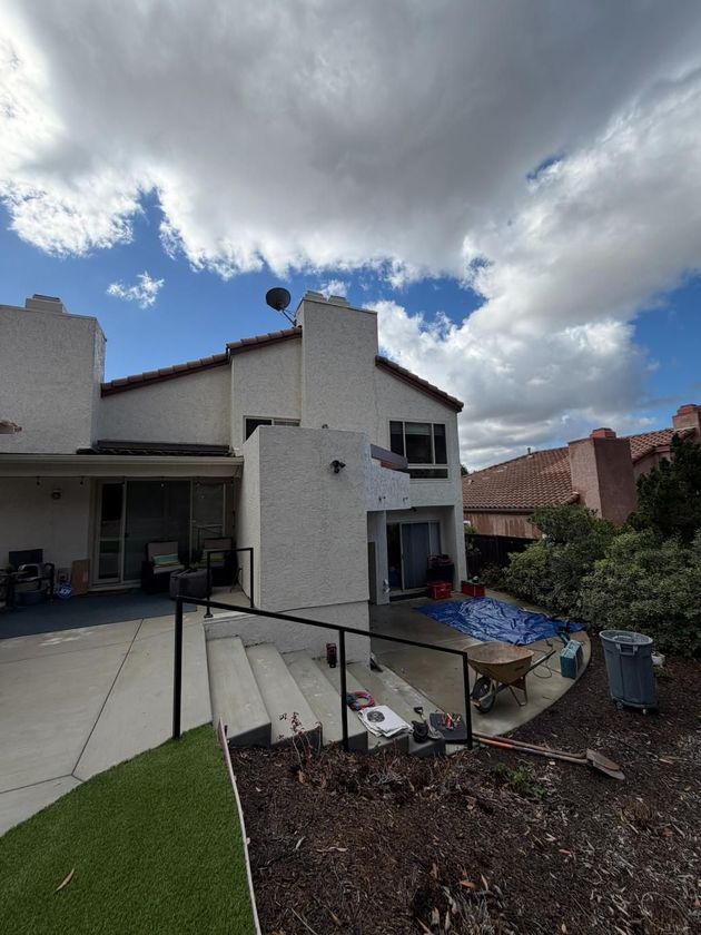 Backyard patio beside a white two-story house under a cloudy sky