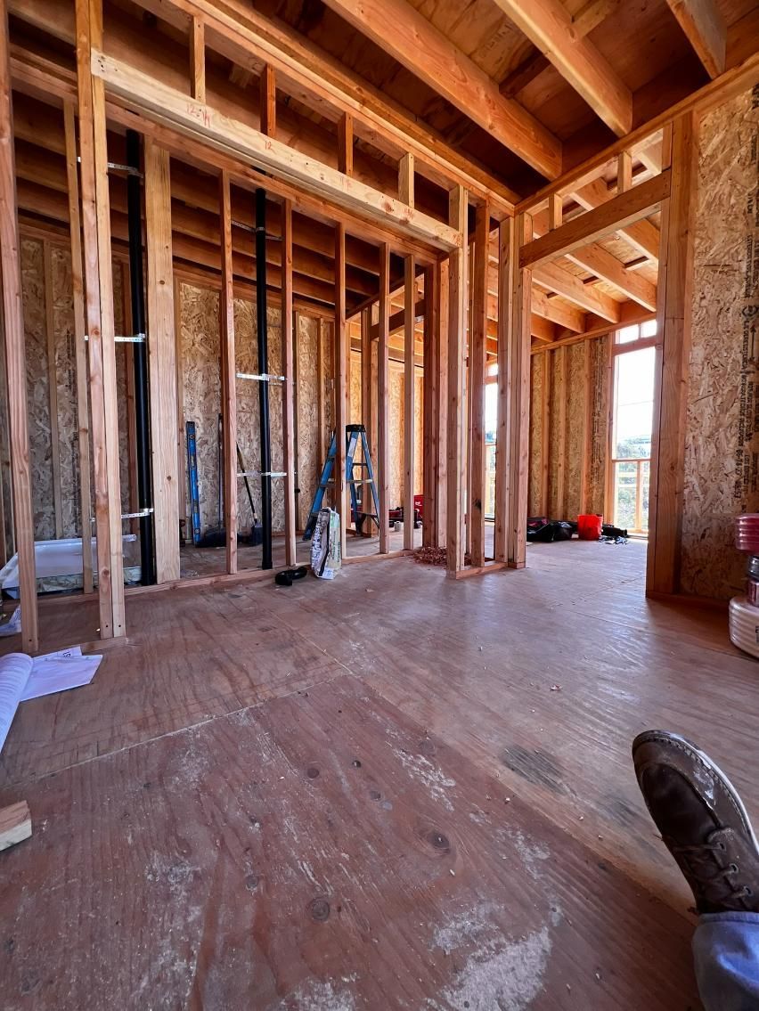 Framed interior of a house under construction with exposed wooden studs and plywood subfloor