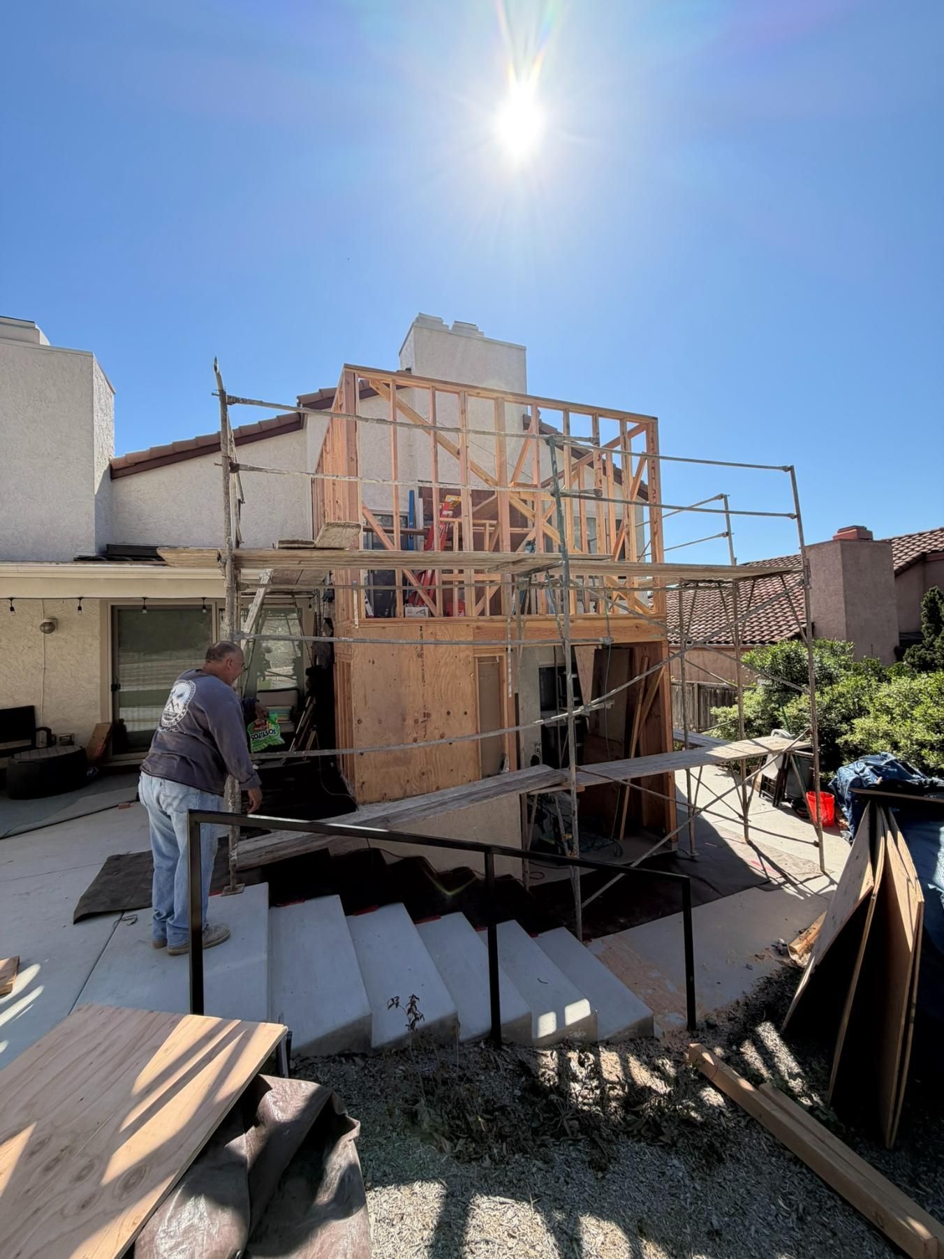 Construction site with wooden framing on a building under a bright sun, worker standing nearby