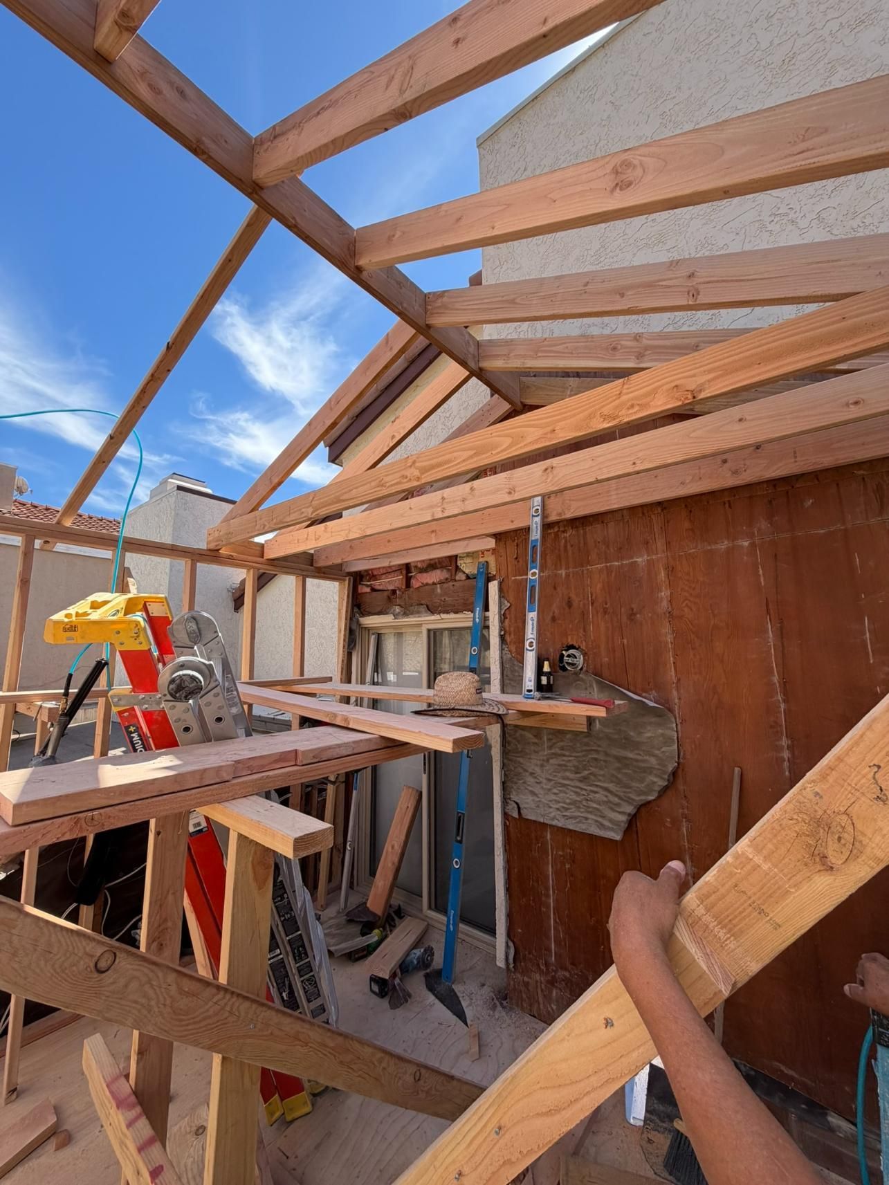 Construction site with wooden roof framing and translucent panels under a blue sky