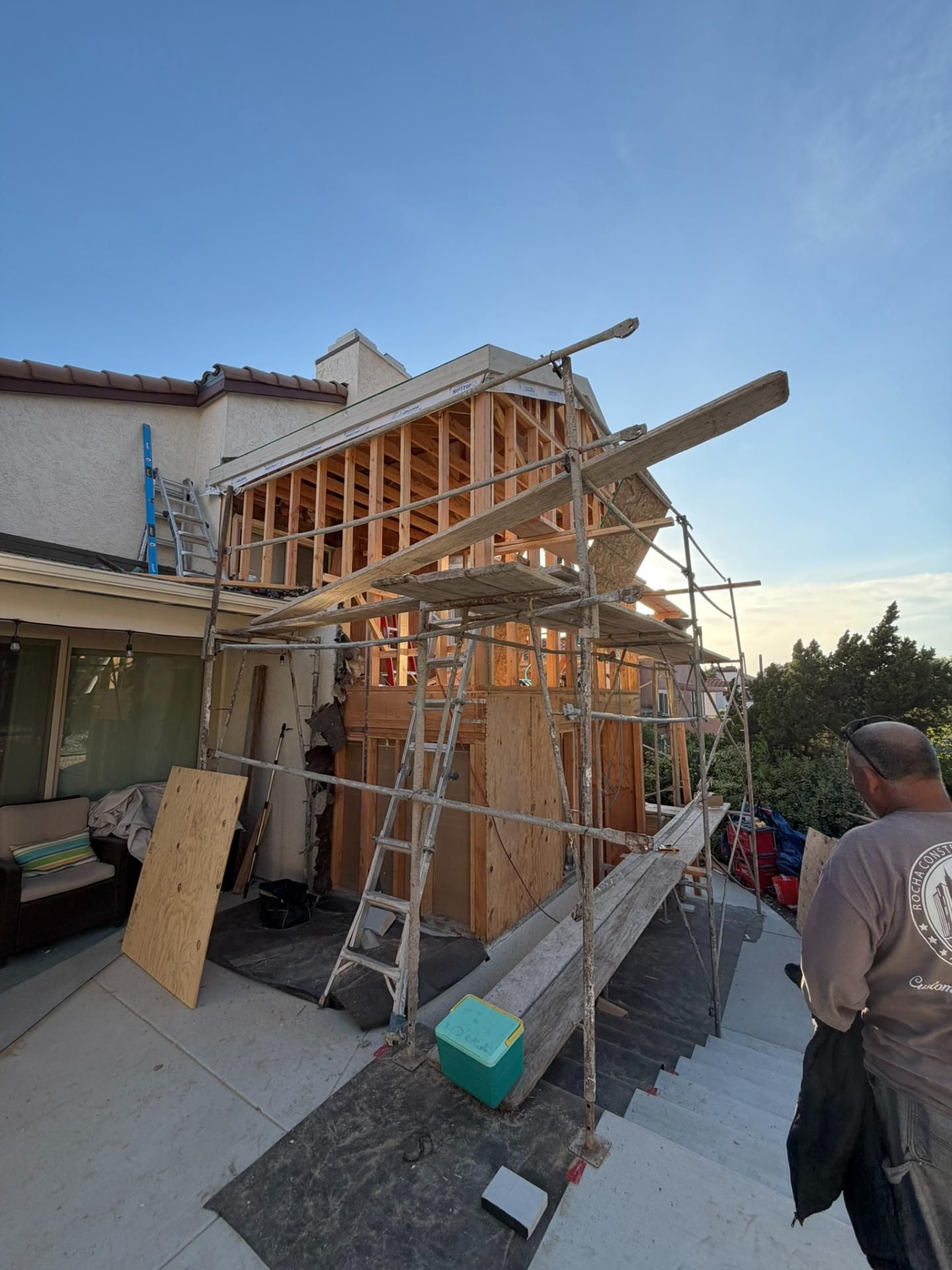 House exterior under renovation with wooden scaffolding and a worker at right at sunset