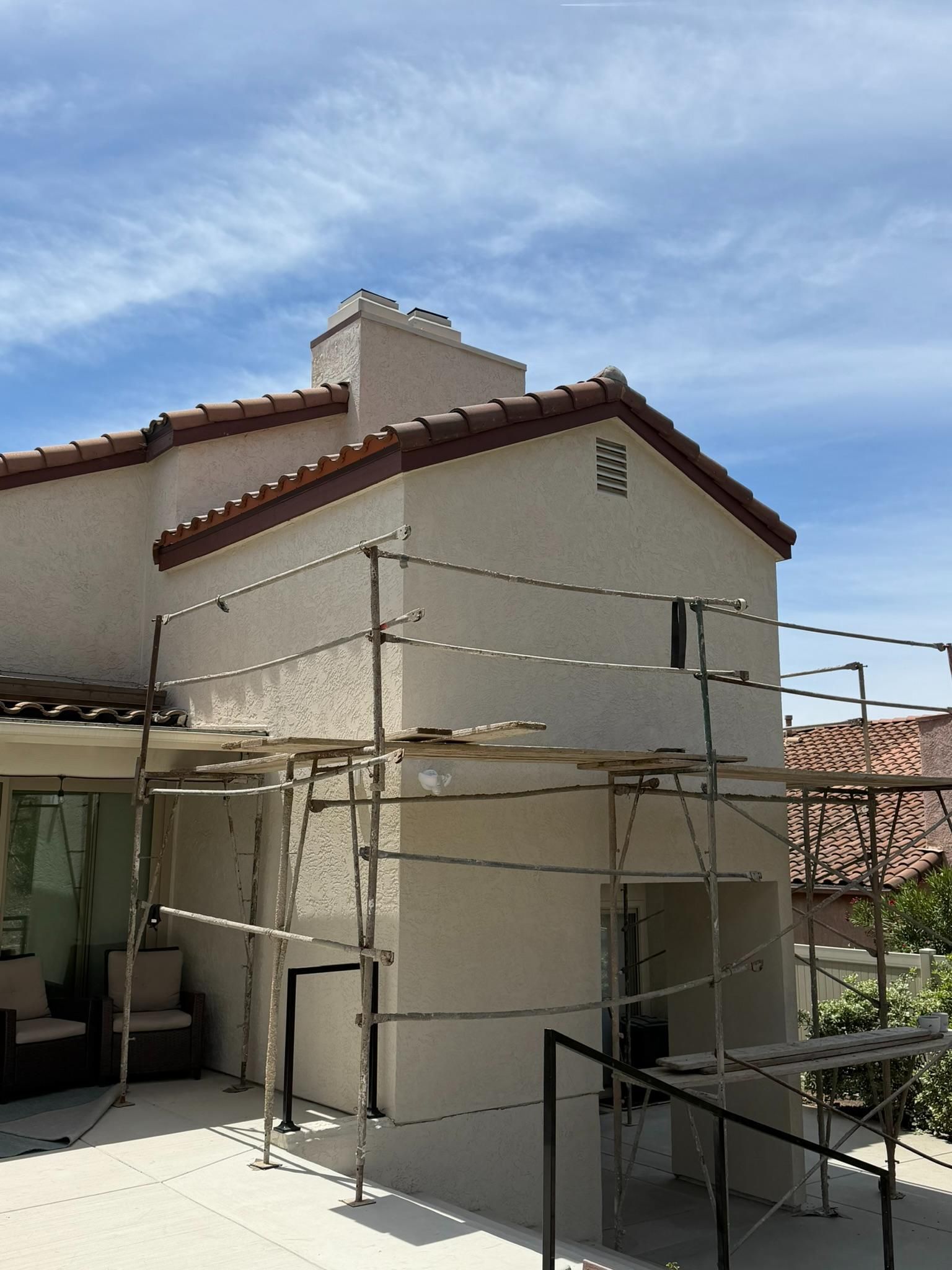House exterior with white stucco walls and red roof tiles, surrounded by scaffolding under a blue sky