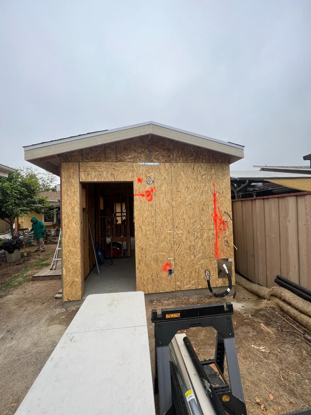 Small unfinished house with a white ramp leading to an open doorway in a dirt yard