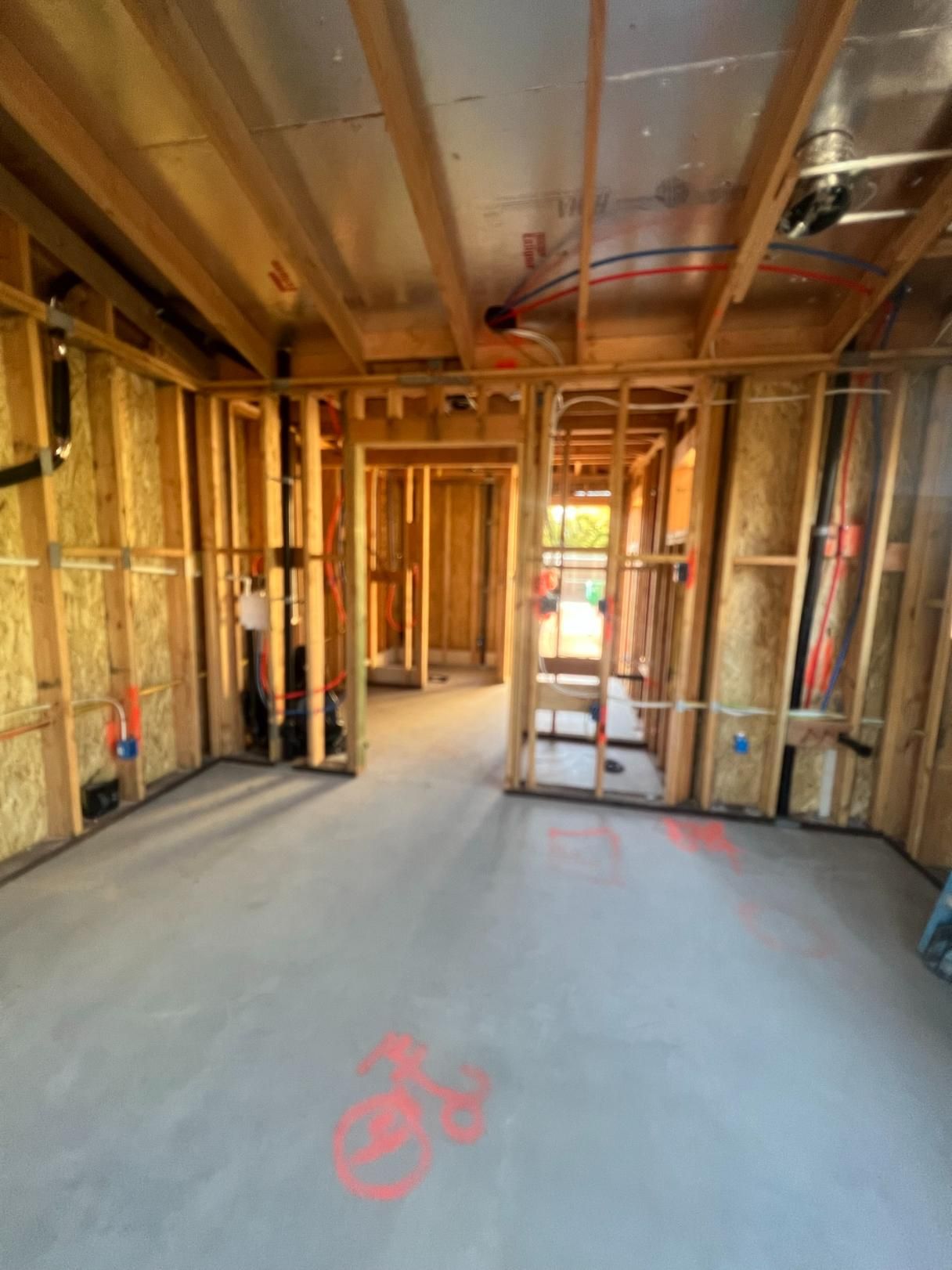 Framed house interior under construction with exposed wood studs, wiring, and unfinished concrete floor