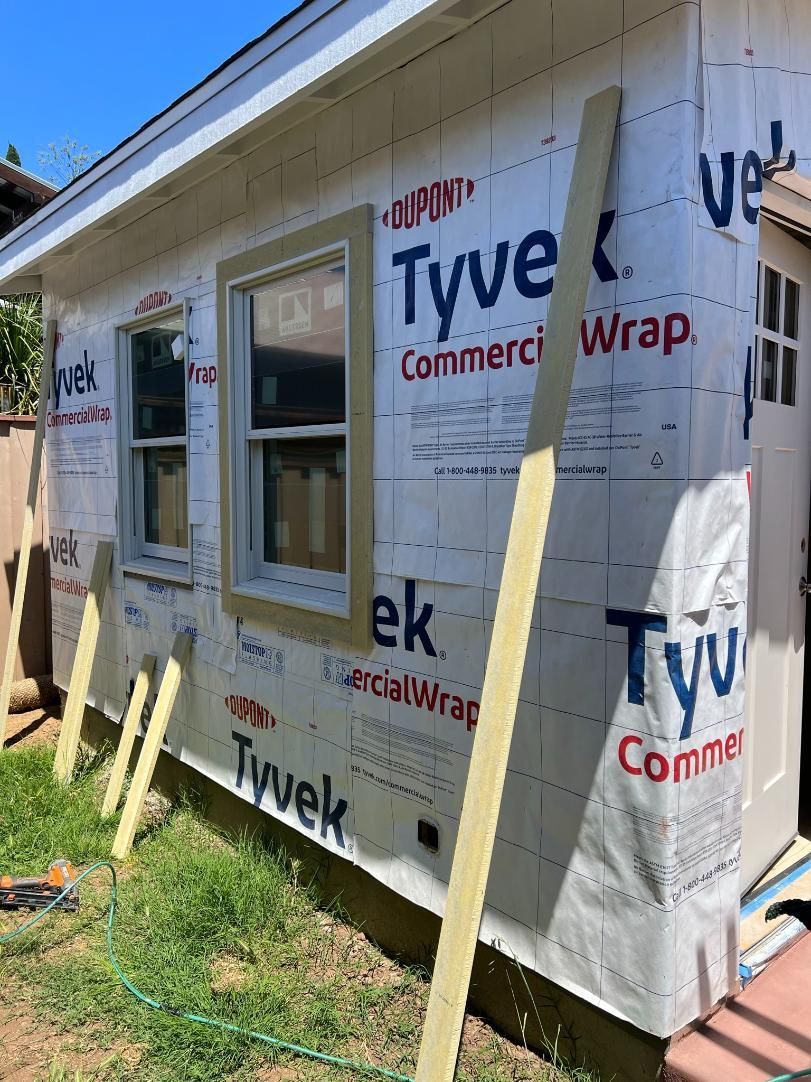 House exterior under construction with Tyvek wrap, windows, and wooden braces.