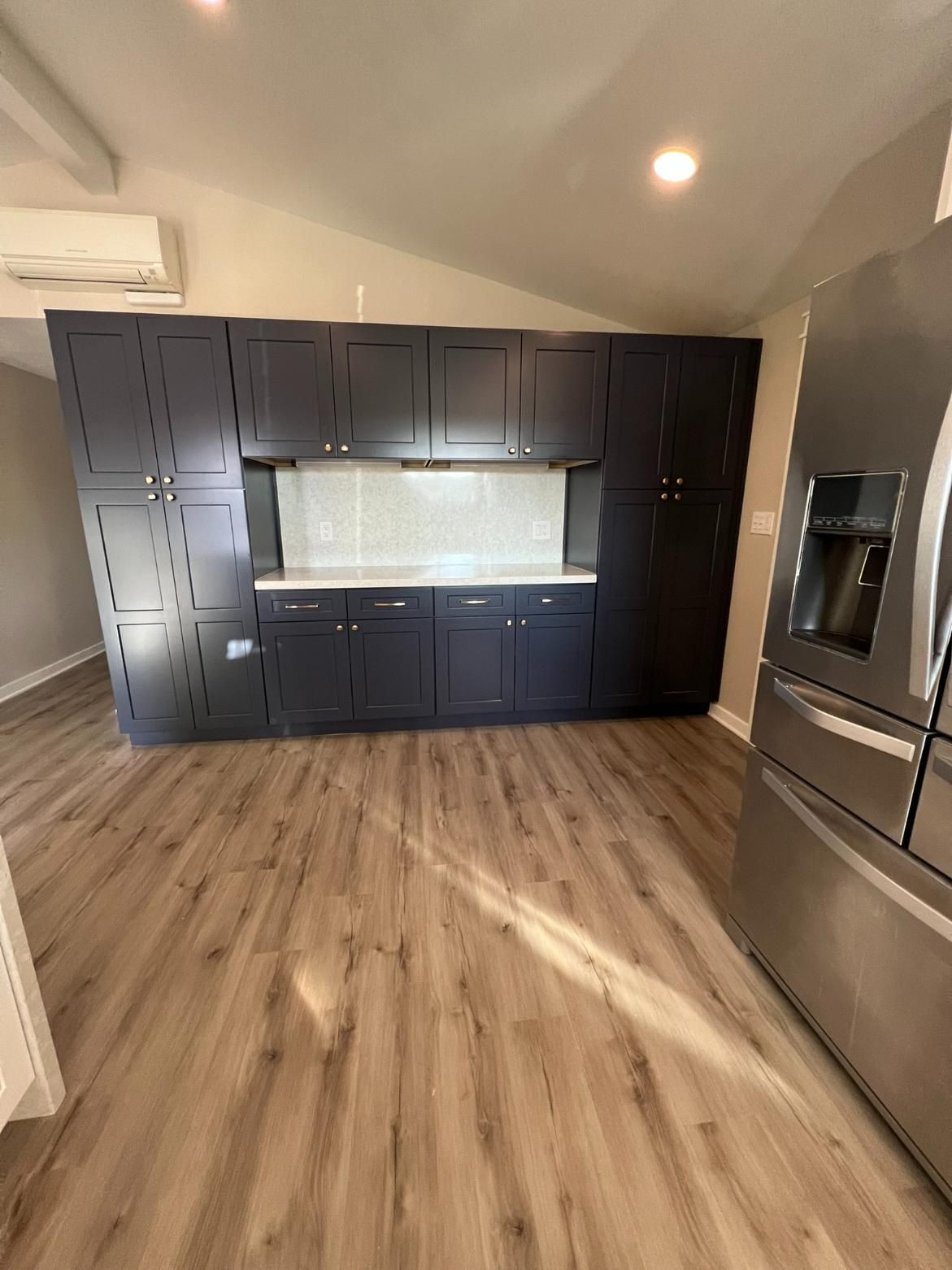 Modern kitchen with dark cabinets, light countertops, stainless-steel appliances, and wood flooring.