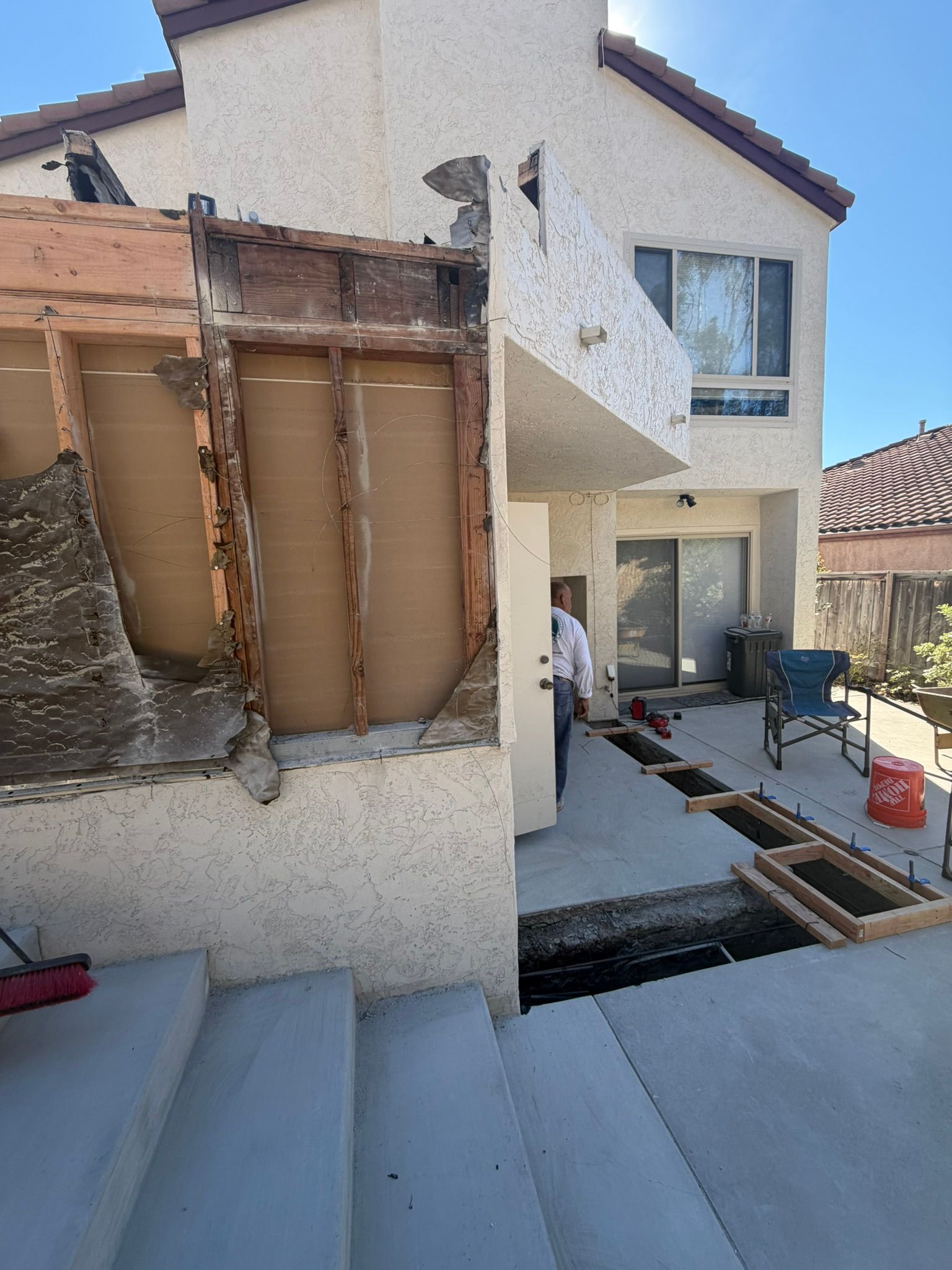 Backyard house under construction with exposed framing, workers, and building materials on the ground.