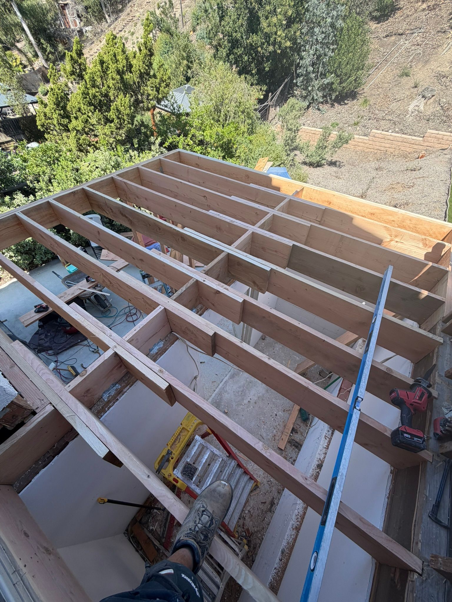 Wooden roof framing under construction, viewed from above with a worker’s boot and tools visible.