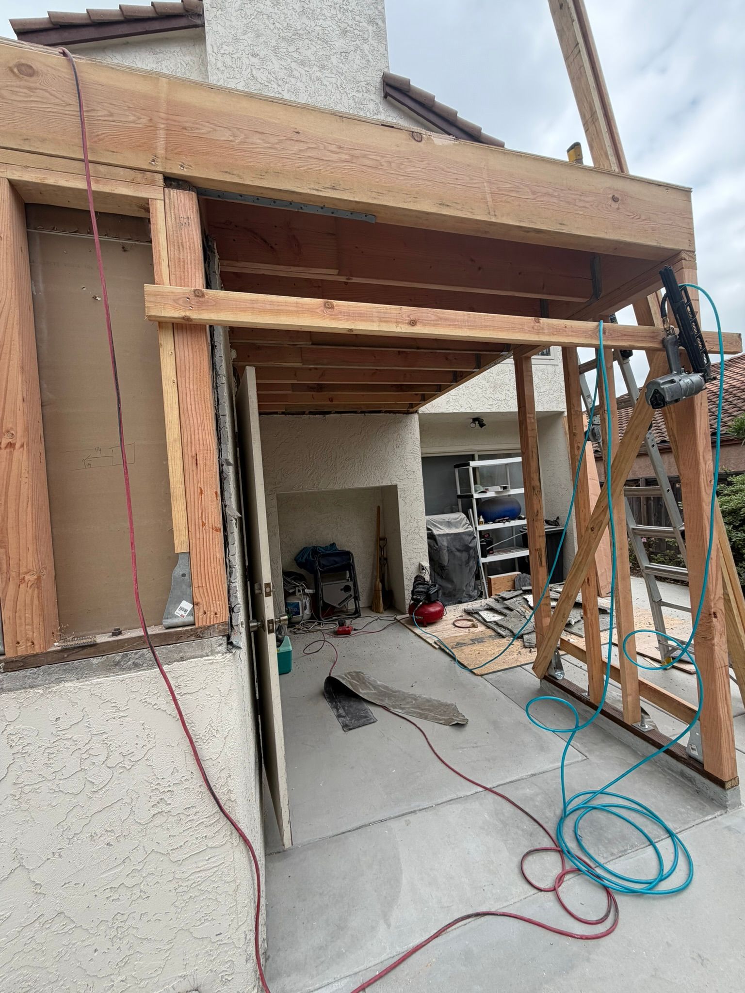 Partially built house entry with exposed wooden framing, tools, and hoses on a concrete floor