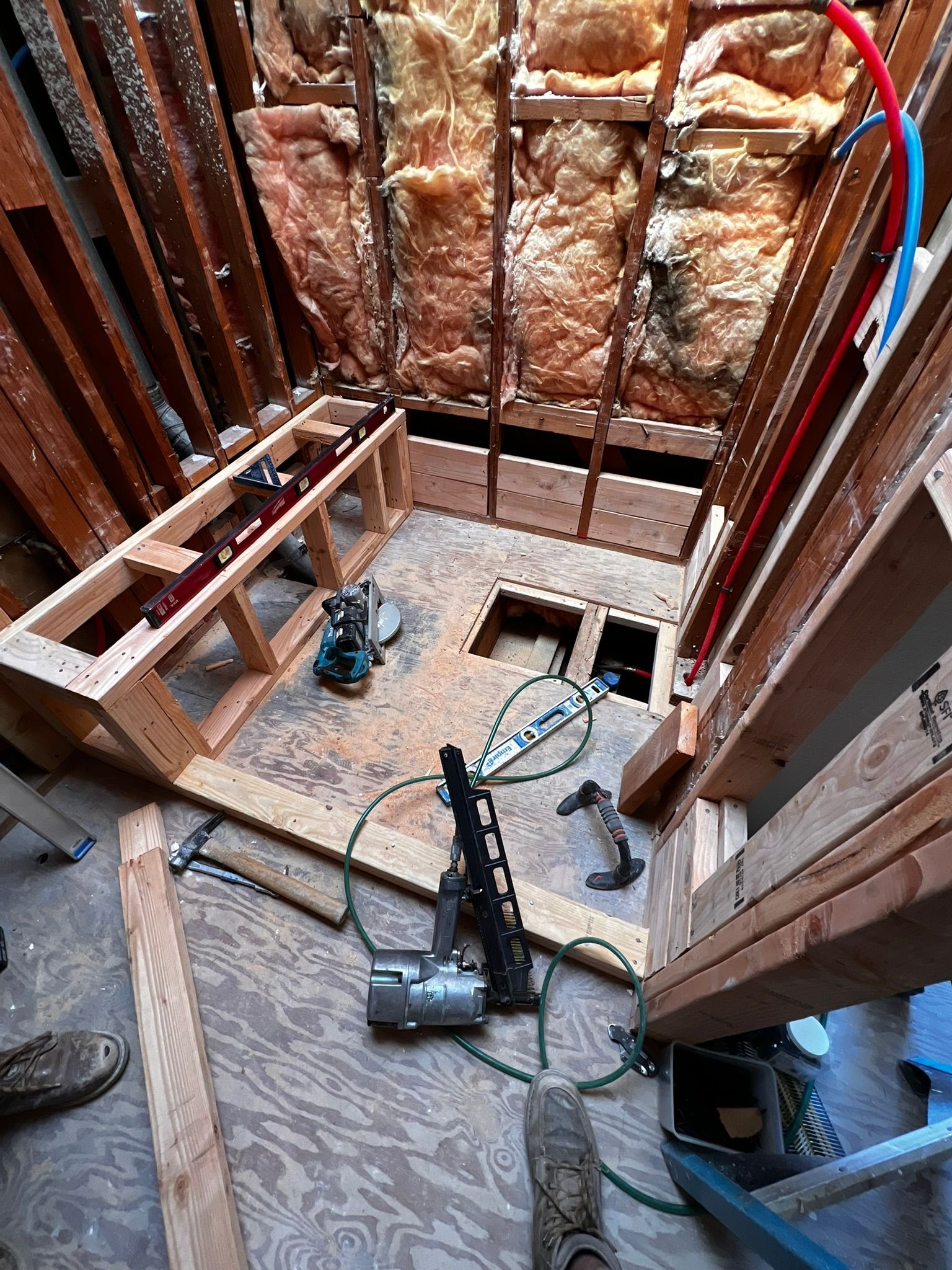 Unfinished basement framed with exposed insulation, tools, and a black shop vacuum on the floor.