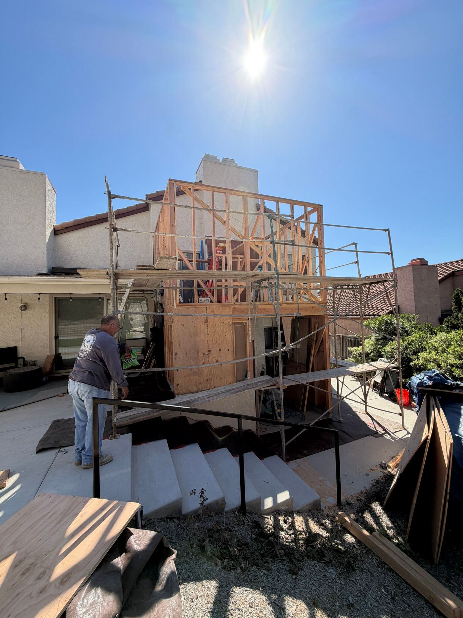 Construction site with wooden framing on a building under a bright sun, worker standing nearby