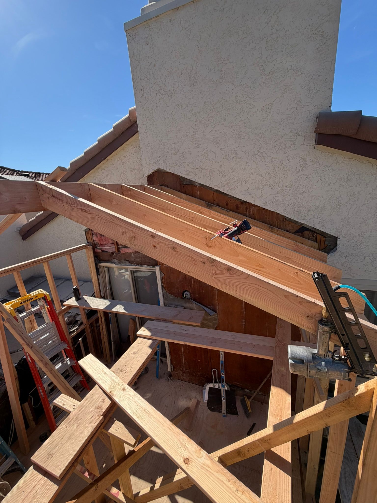 Construction debris and wooden beams piled beside a house under a partly covered roof.