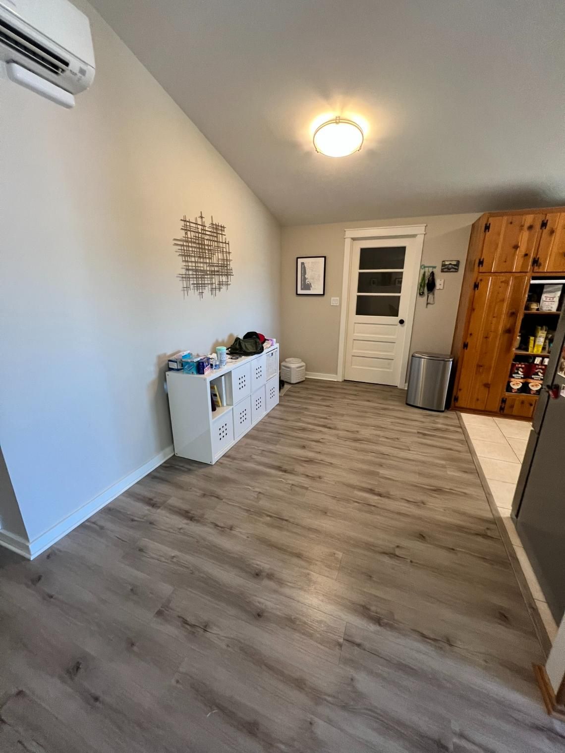 Empty kitchen with gray wood floor, white walls, ceiling light, and a door at the far end.
