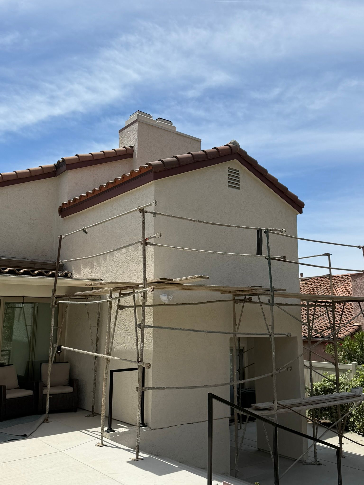 House exterior with white stucco walls and red roof tiles, surrounded by scaffolding under a blue sky