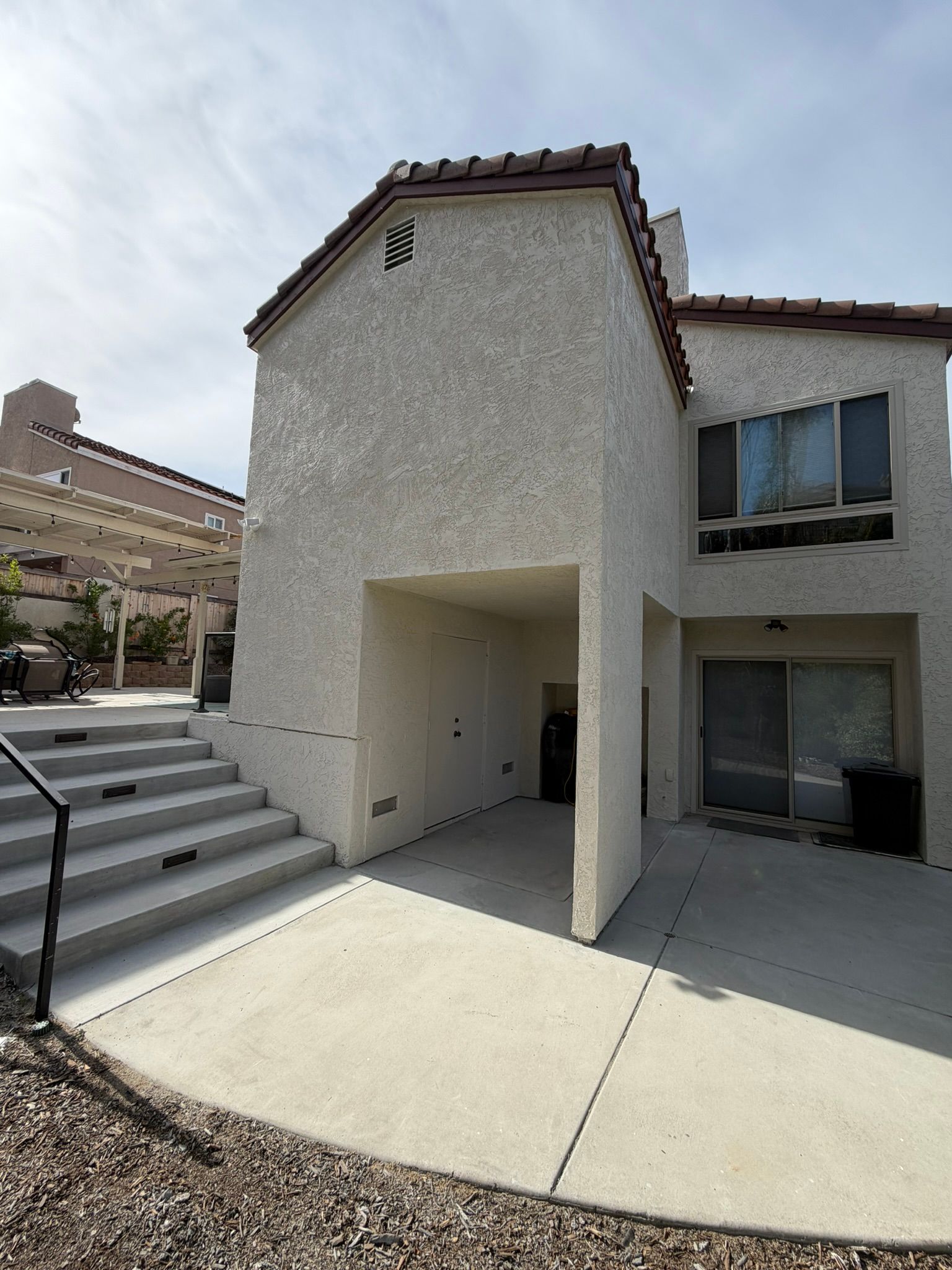 Modern stucco townhouse exterior with covered entry, patio, and stairs under a sunny sky