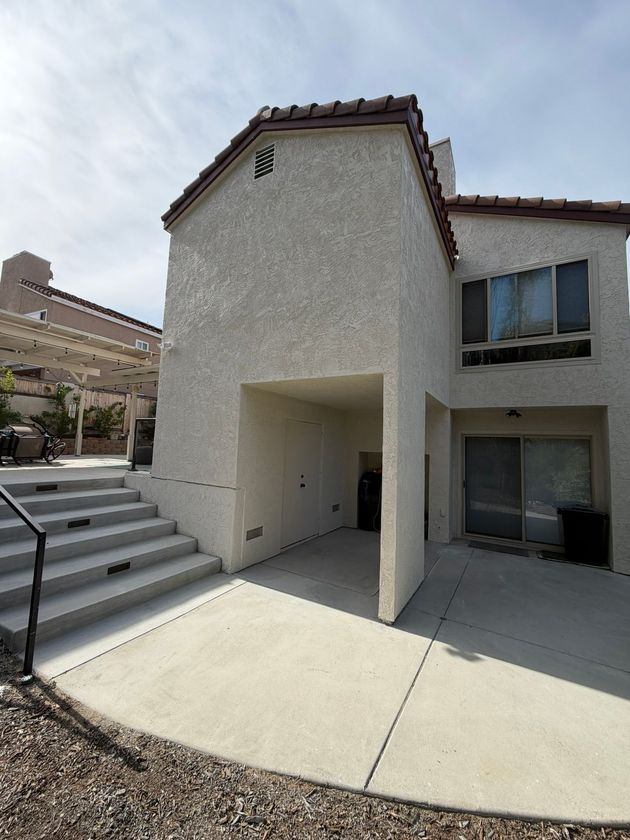 Modern stucco townhouse exterior with covered entry, patio, and stairs under a sunny sky
