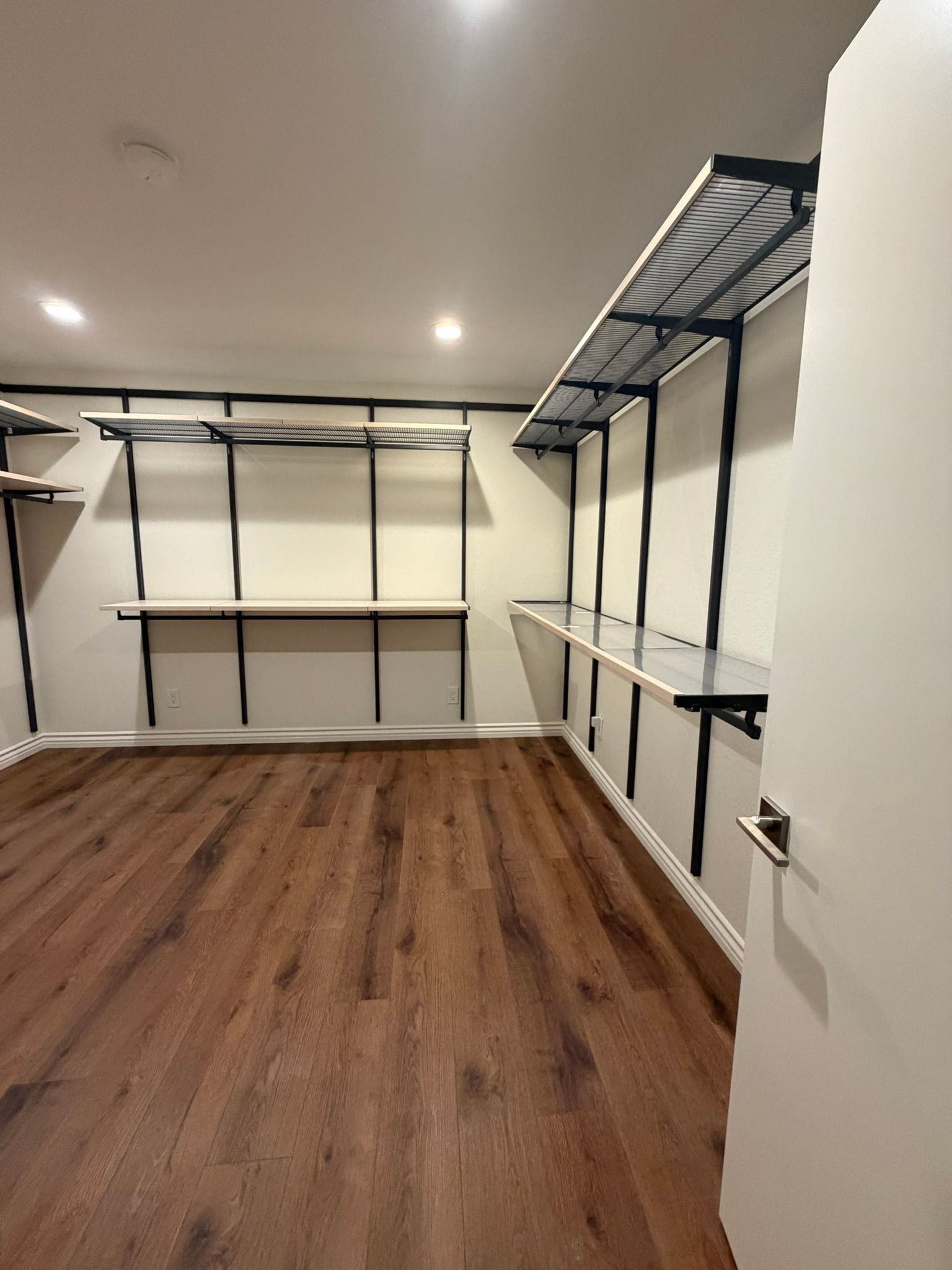 Empty walk-in closet with wood flooring and white walls, featuring black shelving and hanging rods.