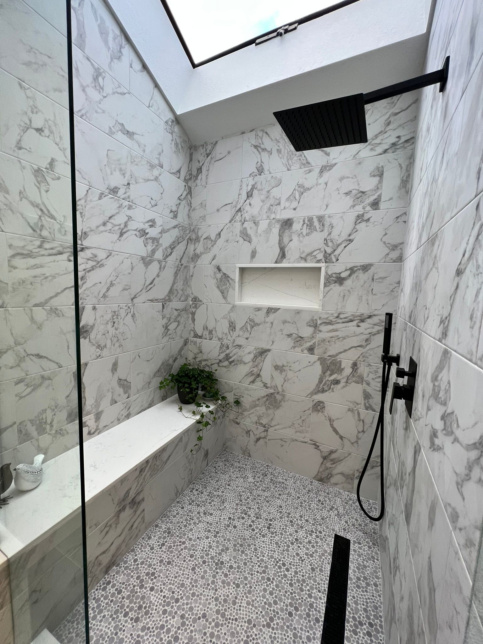 Marble-tiled shower with glass door, black fixtures, and skylight