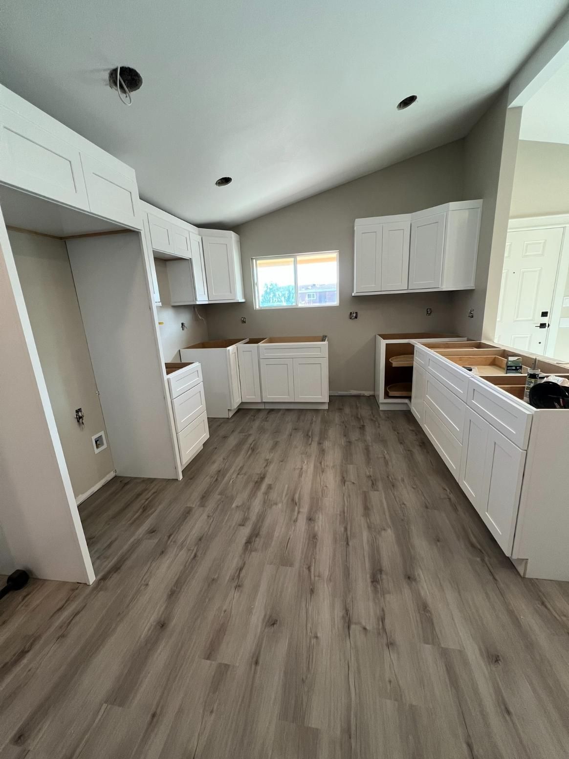 Empty modern kitchen with white cabinets, gray wood floor, and a small window.