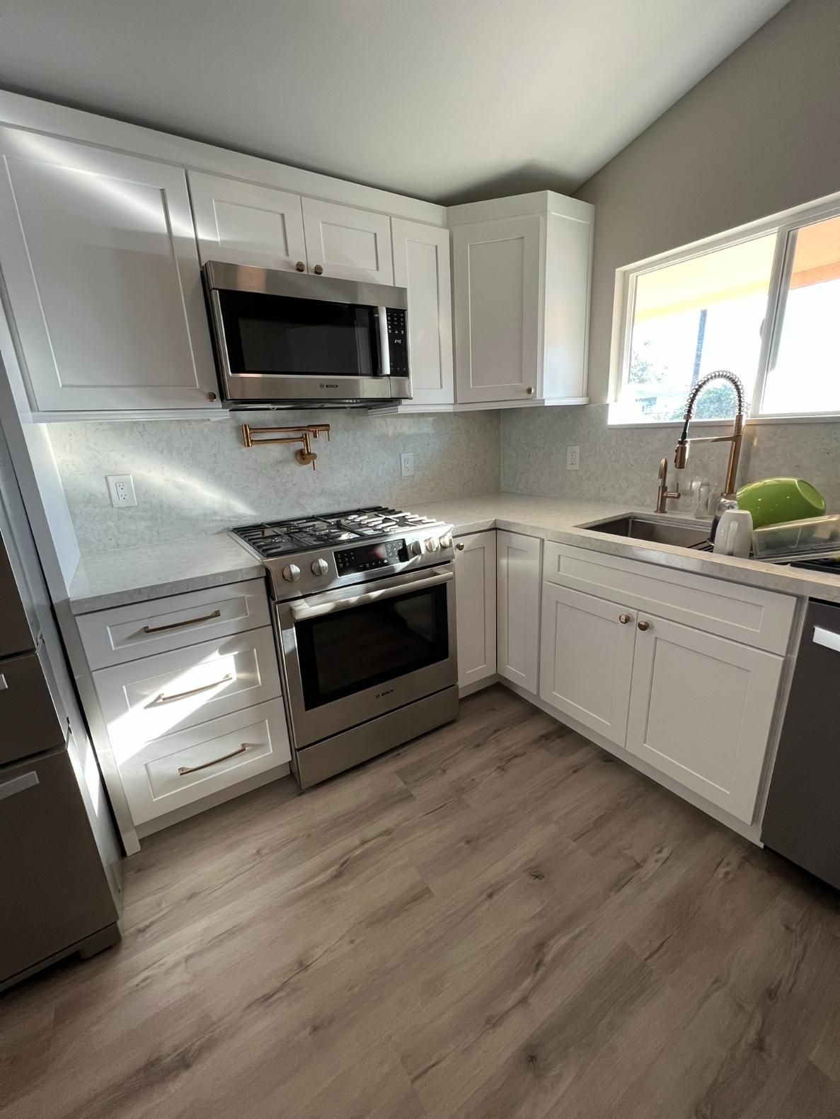Bright white kitchen with stainless steel appliances, gray cabinets, and a sink by a window