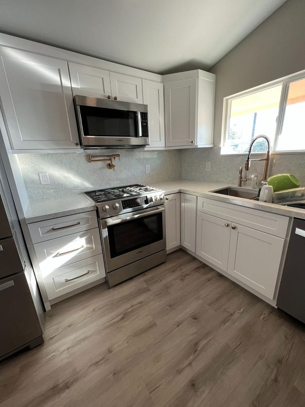 Bright modern kitchen with white cabinets, stainless steel appliances, and a window over the sink