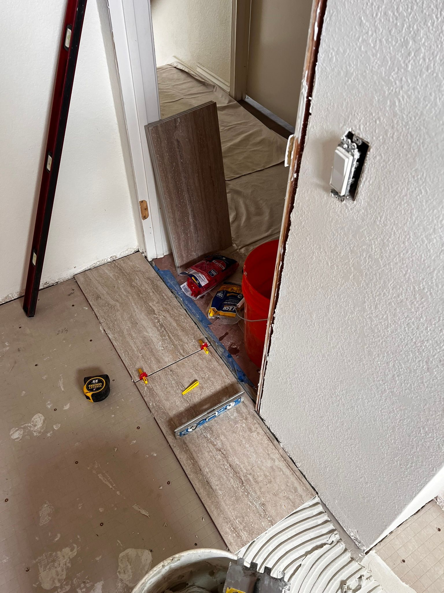 Hallway under renovation with tools, paint bucket, and exposed floor strip near a doorway