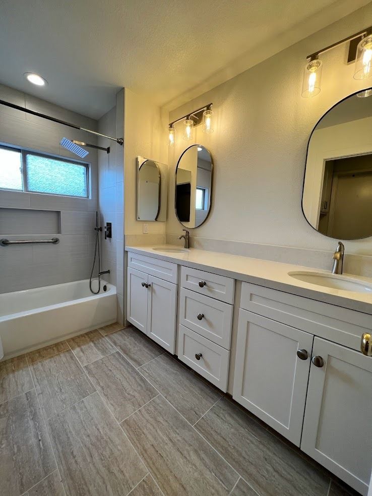 Bright bathroom with white vanity, mirrors, shower-tub combo, and frosted window.