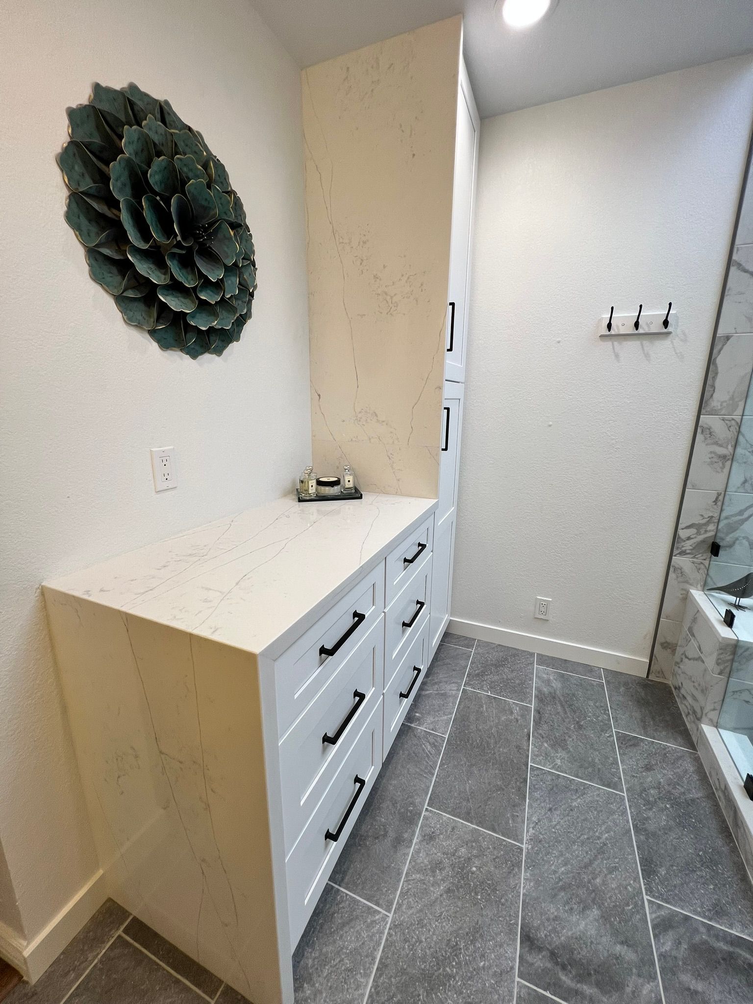Narrow hallway with a white dresser, decorative wall art, and gray tile floor.