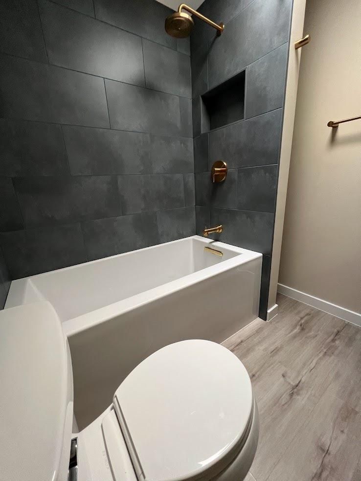 Modern bathroom with a white tub, toilet, dark tiled shower wall, and beige floor.